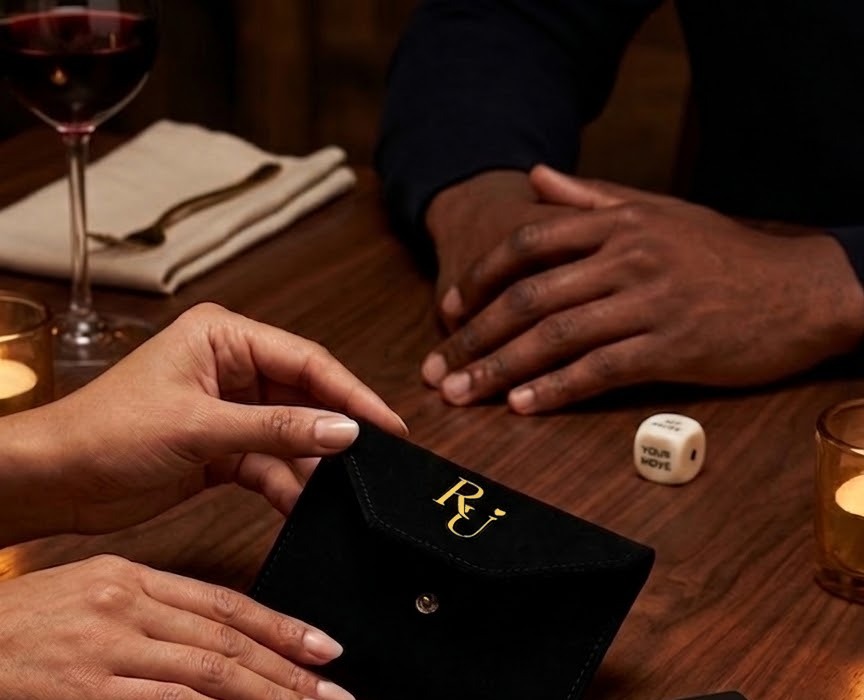 Two people at a candlelit table, one opening the suede pouch, the Chemistry Die resting beside it
